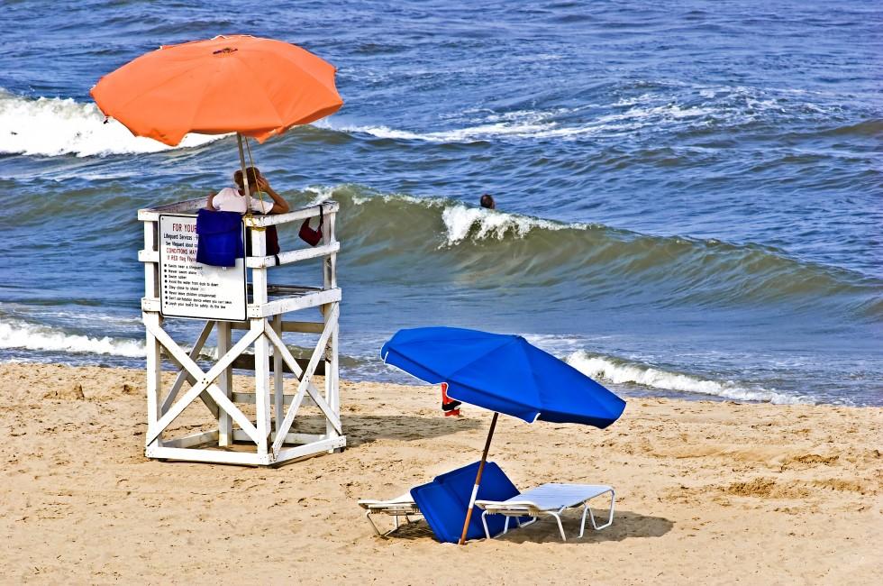 Female lifeguard at her post on Virginia Beach watching a lone swimmer in the ocean surf.