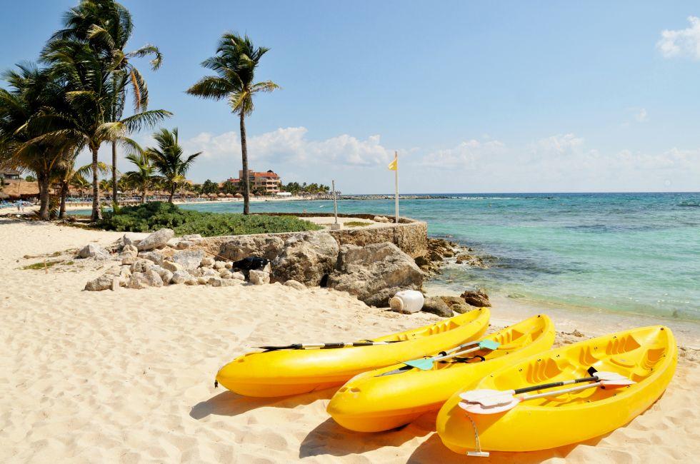 Three yellow kayaks and paddles sit on the tropical white sandy beach town of Riviera Maya, Mexico 