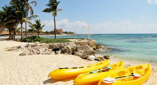 Three yellow kayaks and paddles sit on the tropical white sandy beach town of Riviera Maya, Mexico 