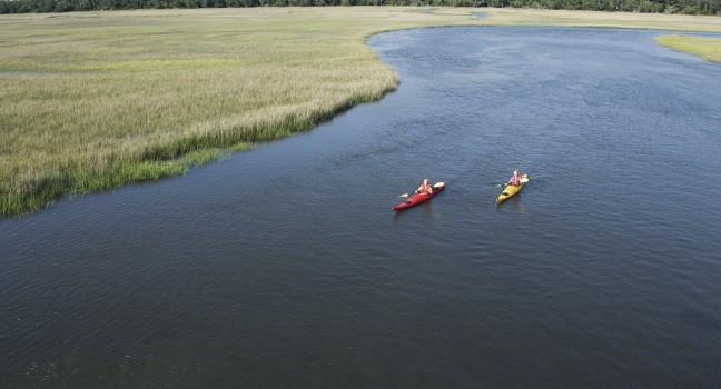Aerial of two teenage boys kayaking through marshland on Bald Head Island, North Carolina.