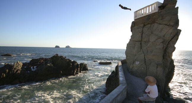 A cliff diver plunges into the pacific ocean.