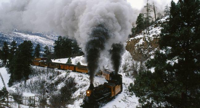 On a wintry curve of iron rails, coal-fired engines cough plumes of smoke and tug their locomotive burden across the Rocky Mountains