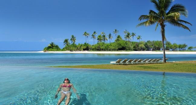 Woman swimming in the infinity pool under the sun in beautiful tropical beach resort in the Bahamas.