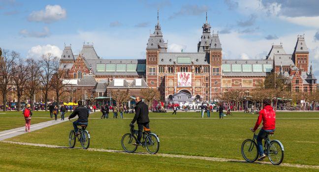 Amsterdam, Netherlands- April 22, 2012: Three men riding their bicycles on a green yard in front of The New Rijksmuseum in Amsterdam.