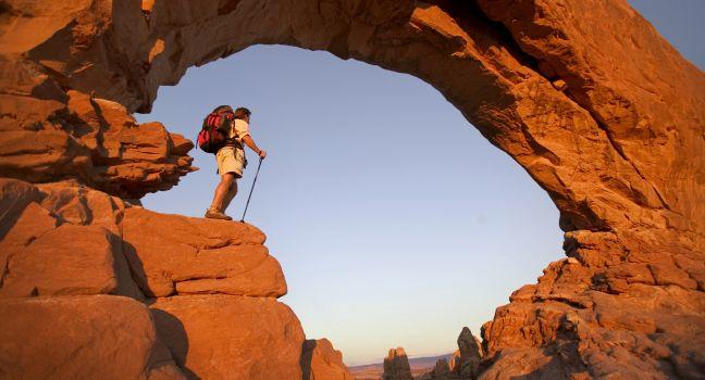 Backpacker standing under magnificent arch in Arches National Park 