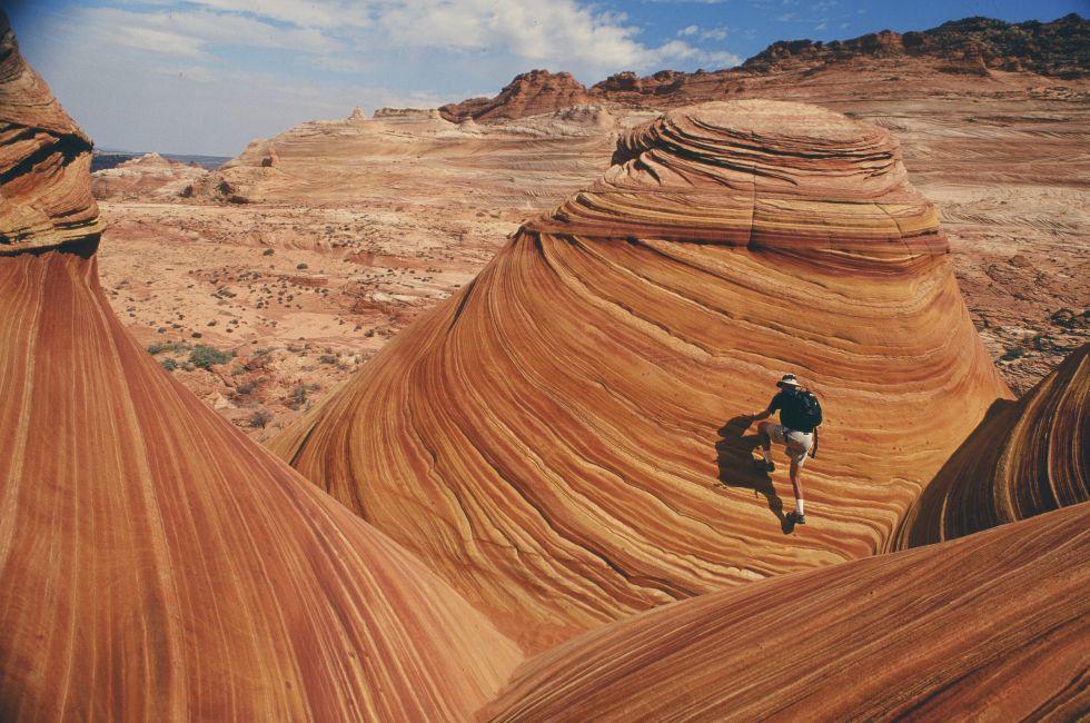A lone hiker explores the astonishing candy stiped sandstone hidden amongst the geologic folds of the Colorado Plateau.