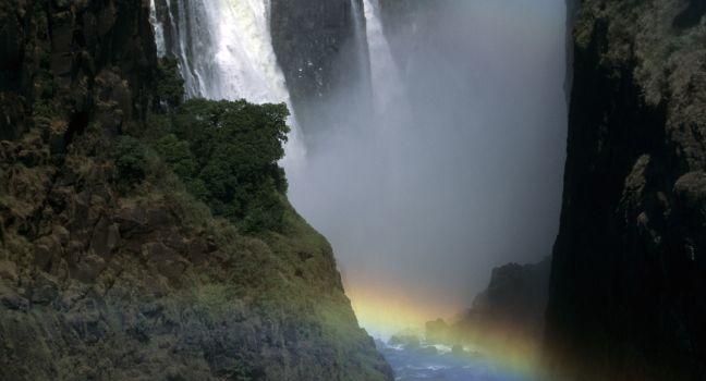 As the Zambezi becomes the world's largest sheet of falling water and grinds a mile-wide basaltic gorge, rainbows crown a thunderous roar, stitching together zambia and Zimbabwe