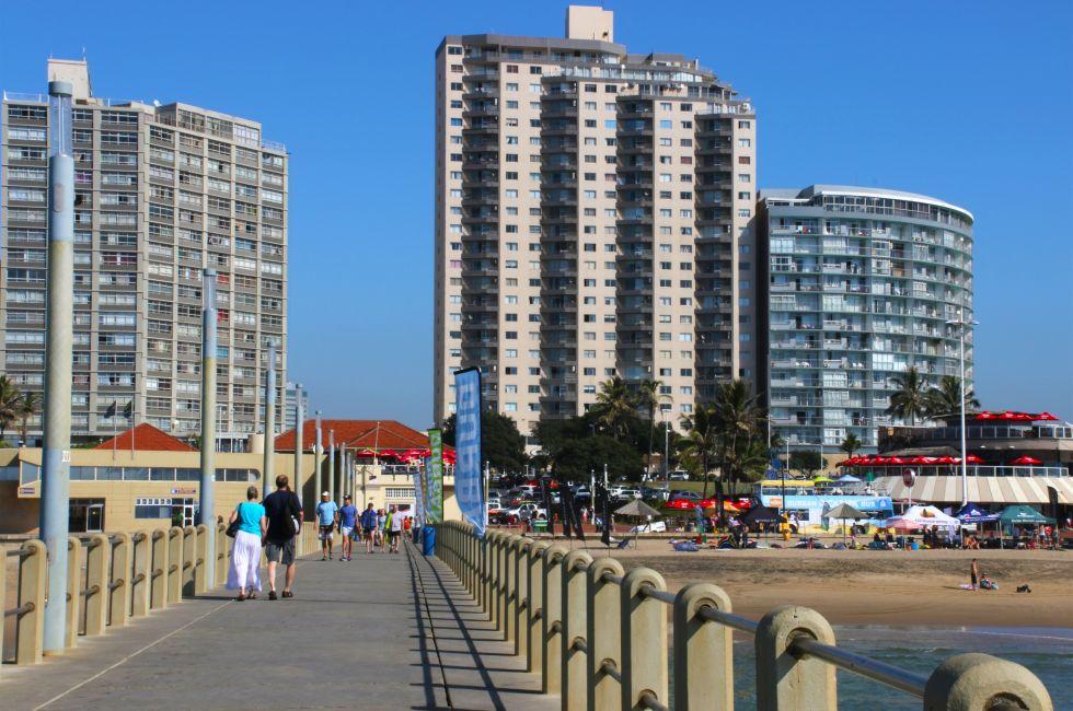 DURBAN; SOUTH AFRICA - MAY 3; 2014: People walk along concrete pier towards commercial and residential buildings on beachfront in Durban South Africa;