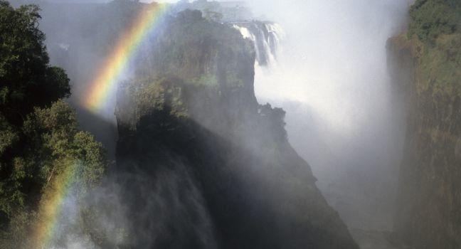 As the Zambezi becomes the world's largest sheet of falling water and grinds a mile-wide basaltic gorge, rainbows crown a thunderous roar, stitching together zambia and Zimbabwe. Victoria Falls, Zimbabwe