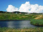A small pond with rolling hills and a big, puffy, cloud in the backdrop. Magdalen Islands.